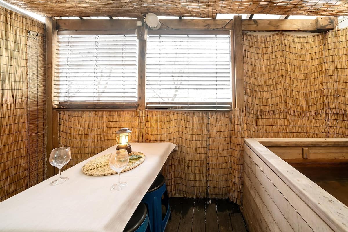 Ein kleiner, rustikaler Raum mit einem Holztisch, einer Bank und einem Fenster mit Jalousien.