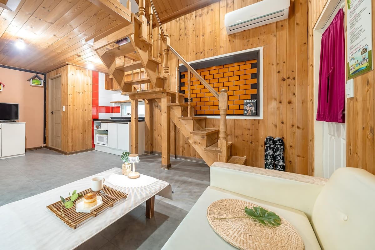 Ein Holzinterieur mit Esstisch, einer Couch, einem Fernseher und einer Treppe.