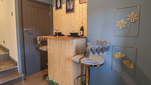 Un espace bar doté d’un comptoir en bois, de deux tabourets de bar rembourrés et d’œuvres d’art encadrées accrochées au mur.