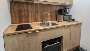 Une cuisine compacte dotée de meubles en bois, d’un évier en acier inoxydable, d’un four à micro-ondes et d’un four encastré.