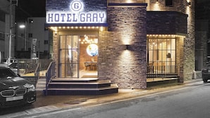 Hotel Gray mit einer markanten, beleuchteten Schrifttafel, einer Ziegel-Fassade und einem sichtbaren Eingangsbereich mit Innenbestuhlung.