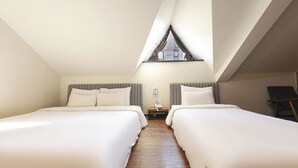Ein Zimmer mit zwei Betten, Holzboden, einem kleinen Tisch mit Telefon und einem Fenster mit Vorhängen.