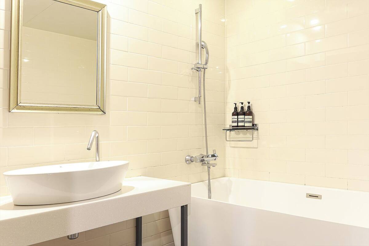 A bathroom with a white sink, a mirror, a shower, and a shelf with toiletries.