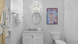 Een badkamer met een wit wastafelmeubel, een spiegel en een toilet. Er hangt een ingelijste poster aan de muur.