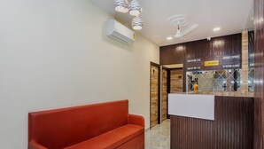 A reception area with a red sofa, a reception desk, a ceiling fan, and an air conditioning unit. - Hotel Good Luck Residency (Mumbai)
