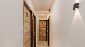 A hallway with wooden doors, a marble floor, and a wall-mounted light fixture. - Hotel Good Luck Residency (Mumbai)