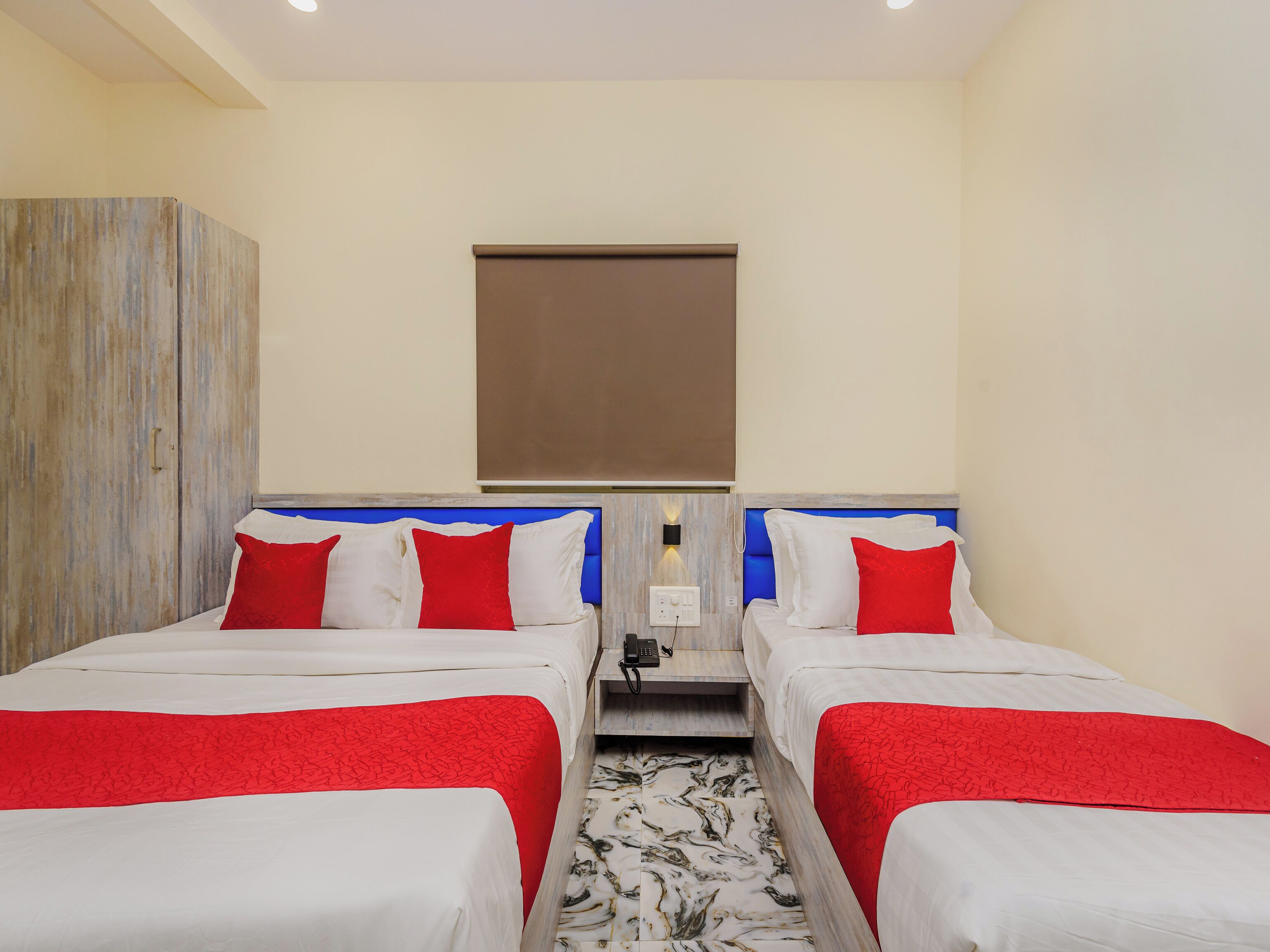 Habitación de hotel con dos camas, cada una con ropa de cama roja y blanca, suelo de diseño marmolado y un armario de madera.
