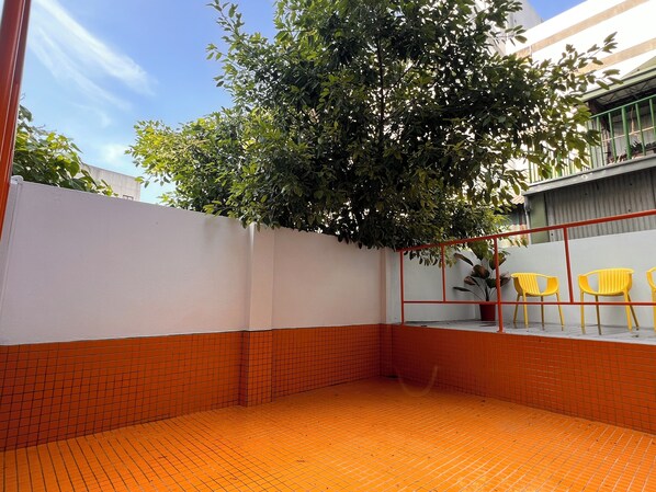 A courtyard with a tiled floor, a white wall, and a tree providing shade. - Mansion122  (Chiayi City)