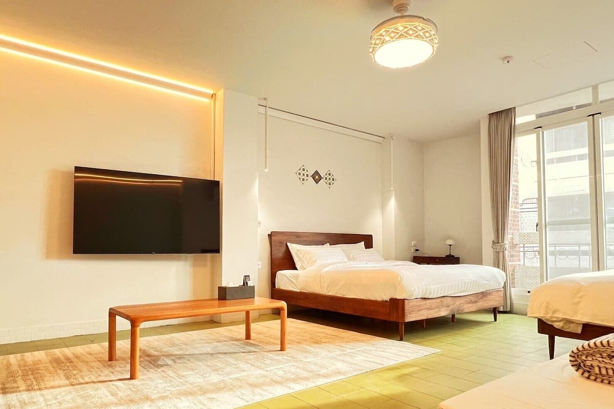 A modern hotel room with a large bed, a bedside table, a TV mounted on the wall, and a view of the city through the window.