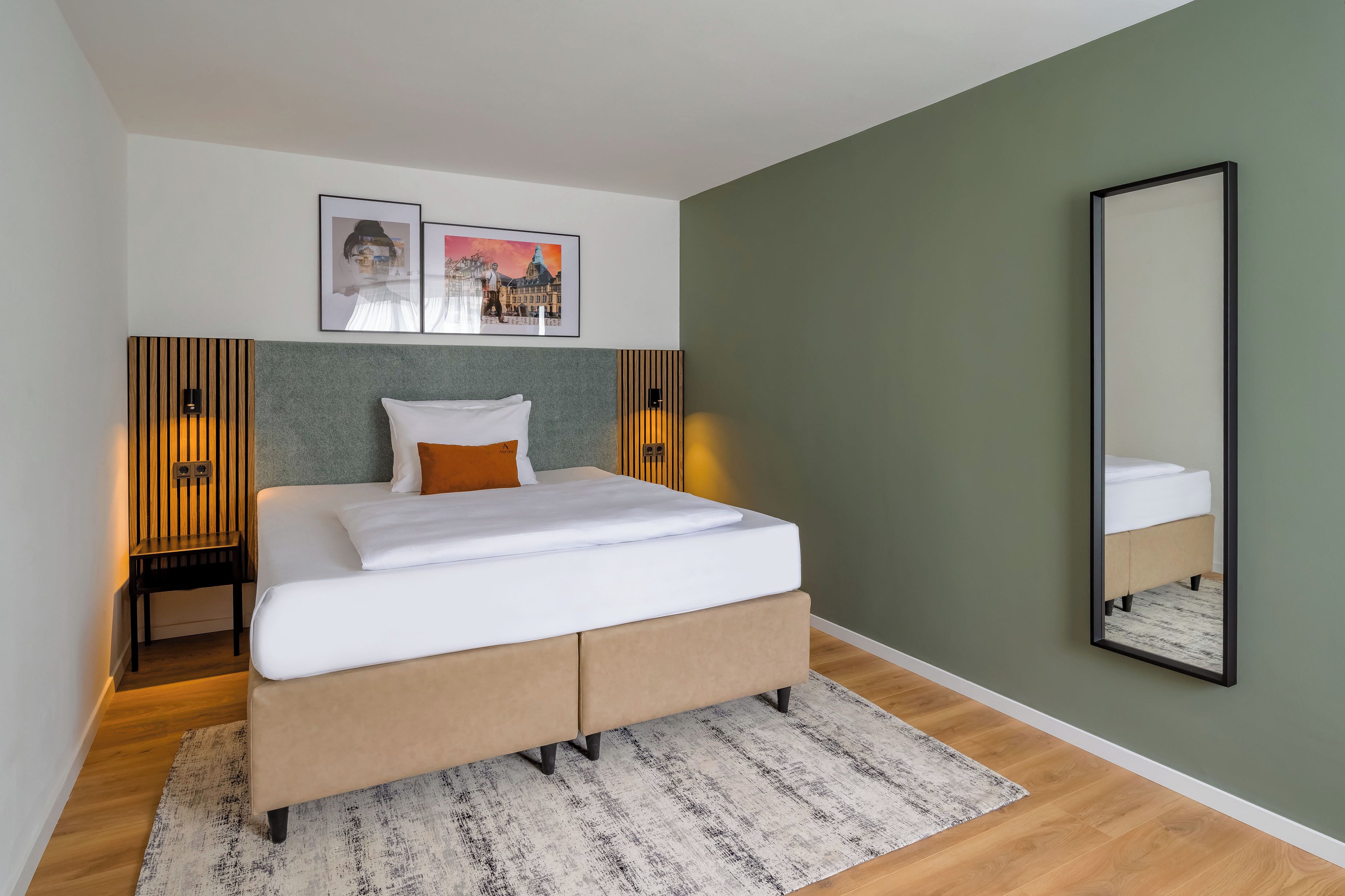 A modern bedroom with a bed, two framed pictures, a mirror, and a nightstand.