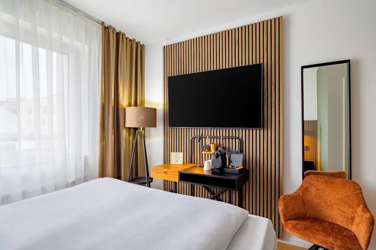Une chambre d’hôtel comprenant un lit, un bureau avec un téléviseur à écran plat, une chaise et un grand miroir.