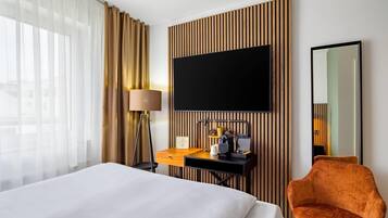A hotel room with a bed, a desk with a flat-screen TV, a chair, and a large mirror.