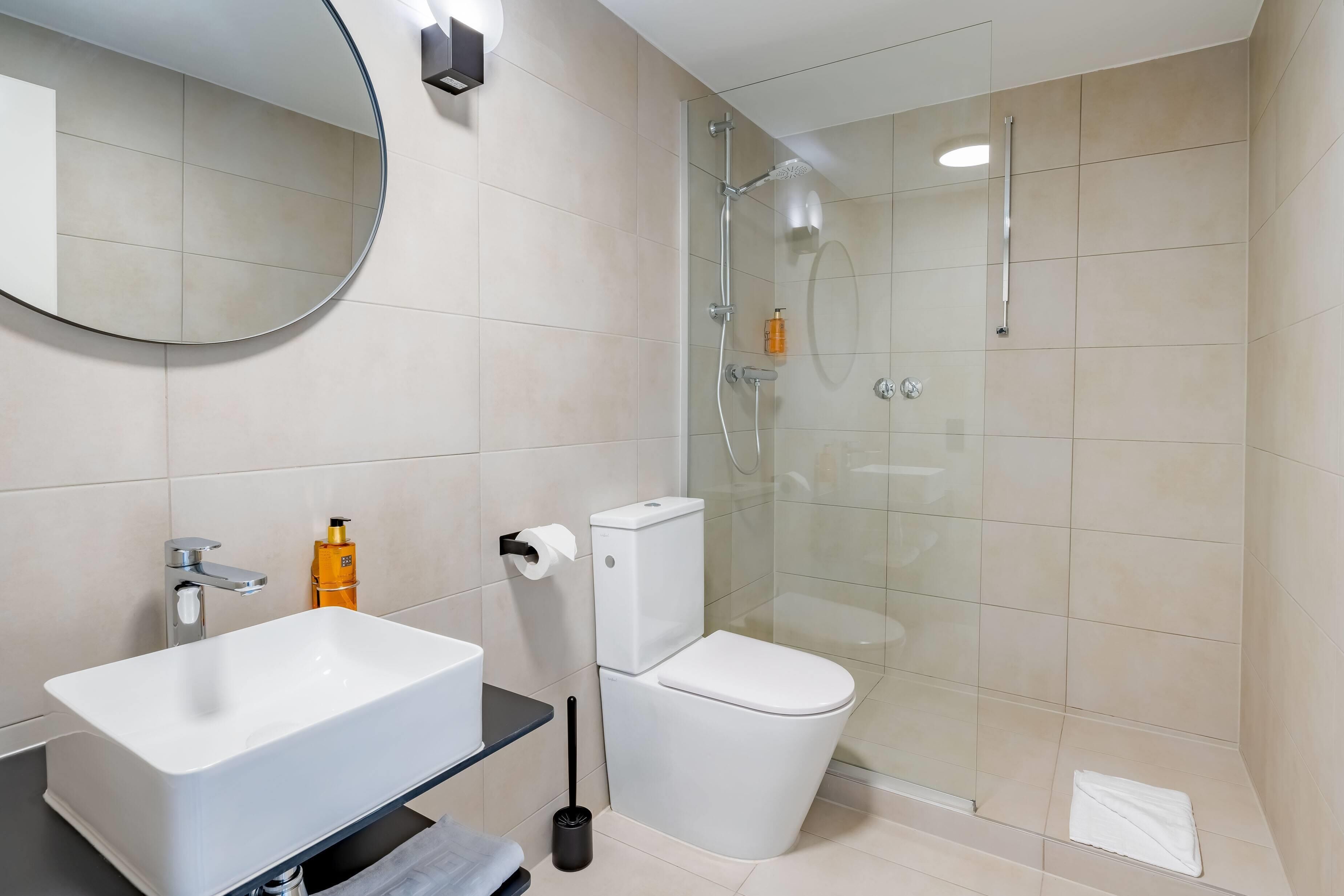 Une salle de bain moderne avec un lavabo blanc, des toilettes et une douche à parois de verre.