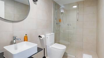 Un baño moderno con lavamanos blanco, inodoro y ducha con mampara de vidrio.