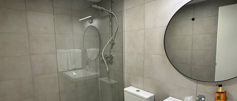 Un baño moderno con ducha envuelta en vidrio, un lavabo blanco y un espejo redondo.