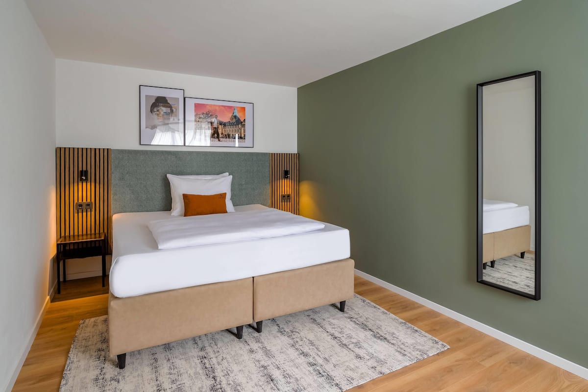 Une chambre à coucher moderne avec un lit, deux tableaux encadrés, un miroir et une table de chevet.