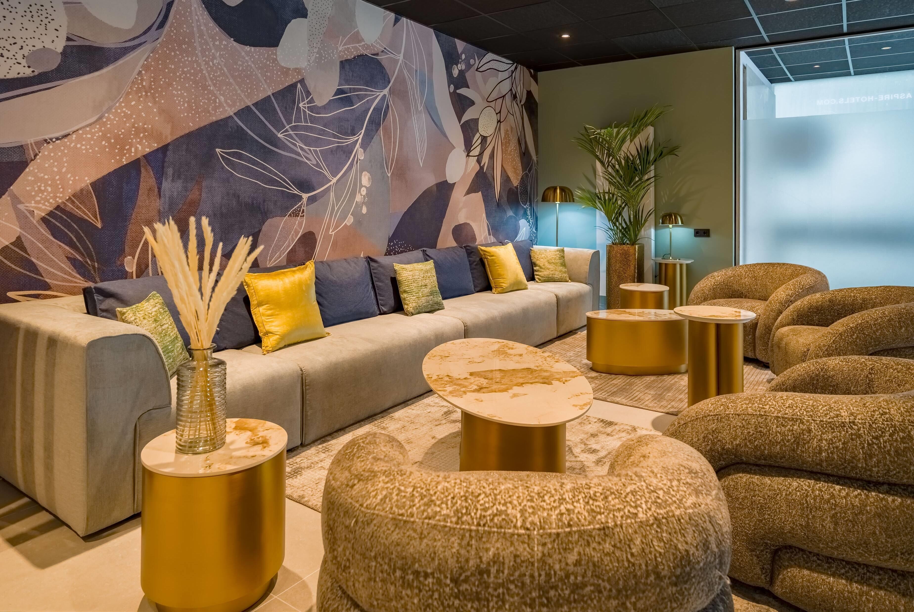A modern lounge area with a sofa, round gold side tables, and textured beige armchairs.