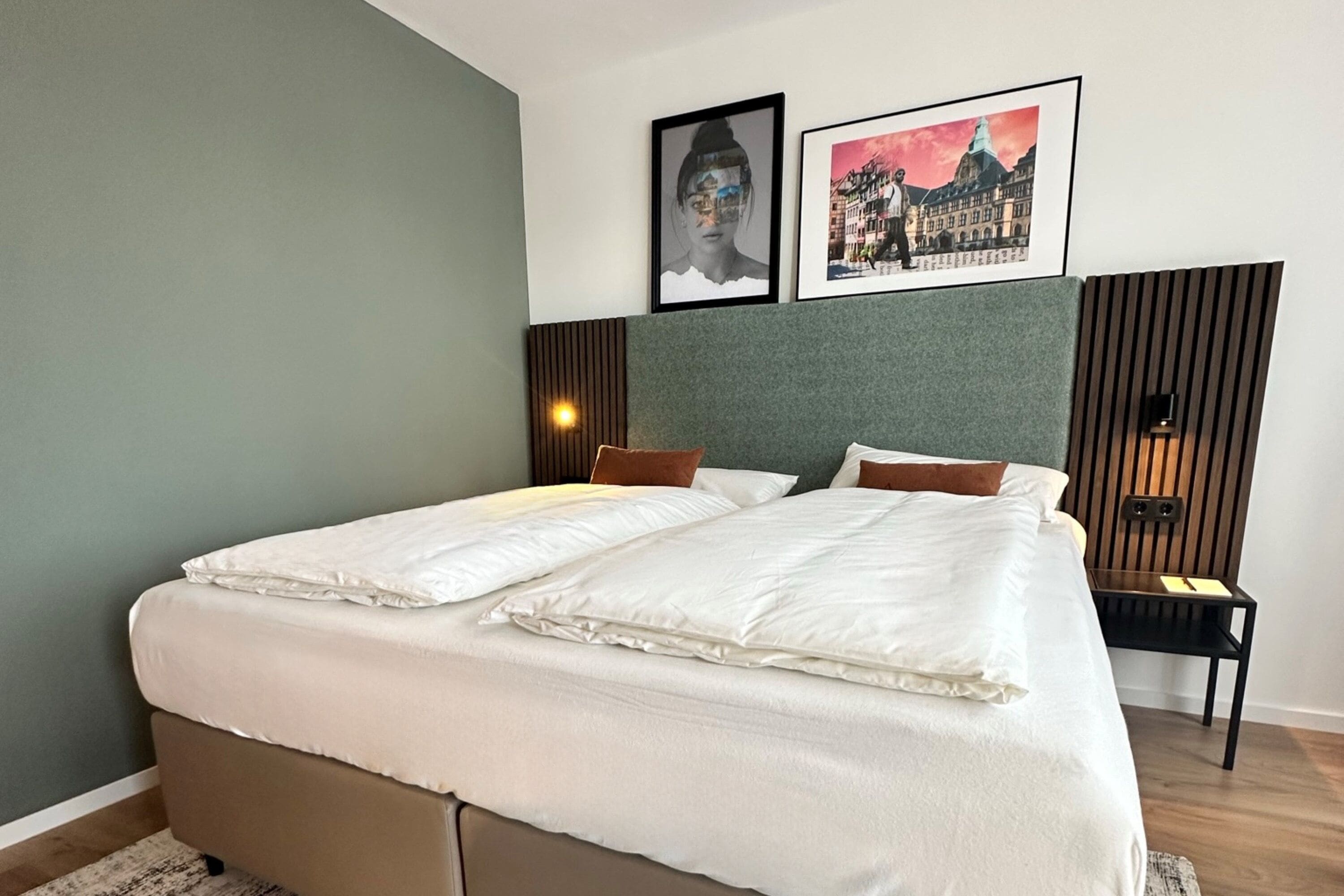 Un lit double avec du linge de lit blanc, une tête de lit avec des lattes de bois verticales et deux tableaux encadrés accrochés au mur.