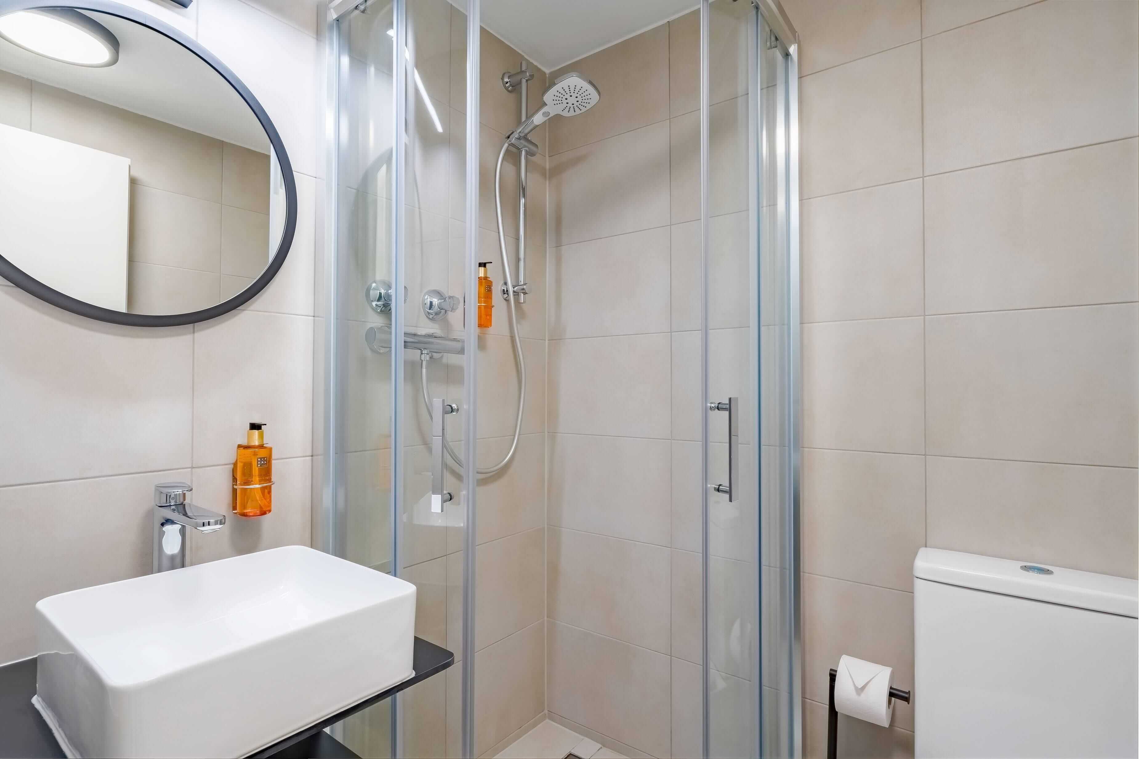Un baño moderno con ducha envuelta en vidrio, un lavamanos blanco y un inodoro.