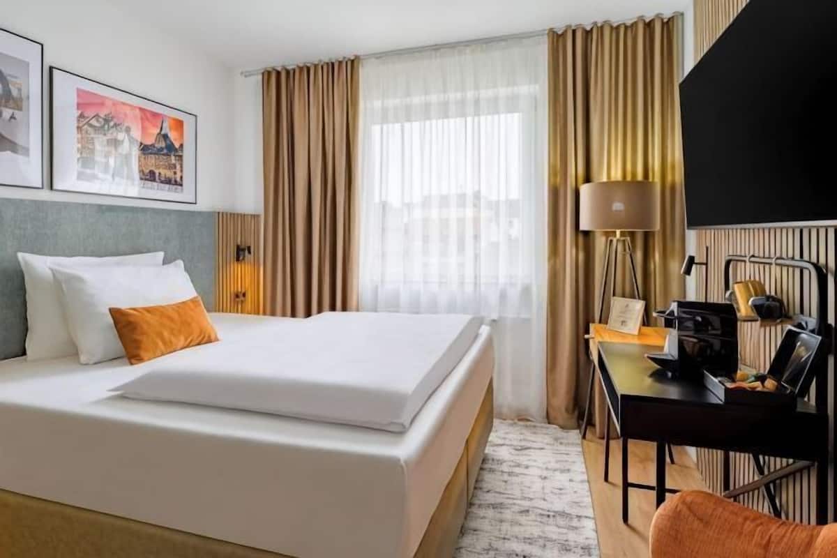 Une chambre d’hôtel avec un lit, un bureau, une lampe et des rideaux.