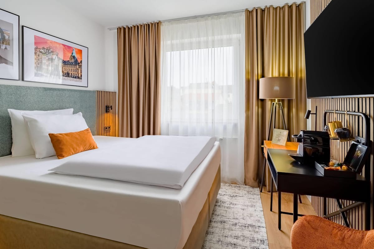 Une chambre d’hôtel avec un lit bien fait, un bureau avec une lampe et une chaise.