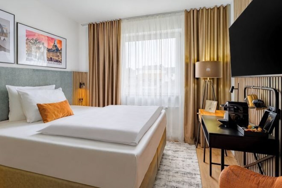 Une chambre d’hôtel avec un lit, un bureau, une lampe et une vue sur la ville.