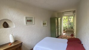 Une chambre avec un sol en briques, un lit avec une literie blanche, une commode en bois et un meuble vert.
