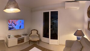 Un salon moderne avec un téléviseur, un canapé et un coin repas comprenant une table et des chaises en bois.