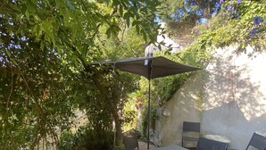 Une terrasse extérieure avec une table et des chaises, entourée de verdure et d’un mur.
