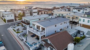 Een kustgebied met woonhuizen, moderne woningen, een opvallend huis met balkon en uitzicht op de oceaan bij zonsondergang.