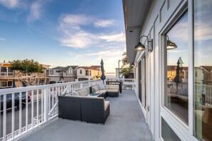 Ein Balkon mit Sitzgelegenheit im Freien, Geländer und Blick auf das Meer und umliegende Gebäude.