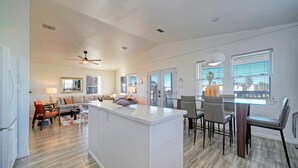 A spacious living area with a central island, a dining area with a glass table, and a kitchen with a white refrigerator. - Private Pool, in Golf Cart Zone, Golf Cart for Rent | Sea Therapy by AvantStay (Port Aransas)