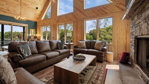 A spacious living room with a high ceiling and large windows, featuring leather sofas and a fireplace. - The Lodges | AvantStay | Lakefront, Sleeps 66 | Pools, Docks, Theaters, Views (Sherrills Ford)