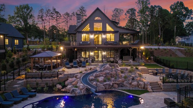 A two-story house with a large front deck, a swimming pool, and a stone waterfall feature. - The Lodges | AvantStay | Lakefront, Sleeps 66 | Pools, Docks, Theaters, Views (Sherrills Ford)