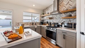 A modern kitchen with a central island, built-in oven, microwave, and stainless steel appliances. - Montego by AvantStay | Private Yard w/ Pool & Hot Tub (Indio)