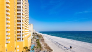 Un hotel moderno con balcones, una playa y un cielo azul despejado.