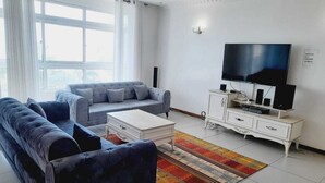 Un salon moderne comprenant un grand ensemble de canapés, une table basse, un téléviseur et un meuble blanc.