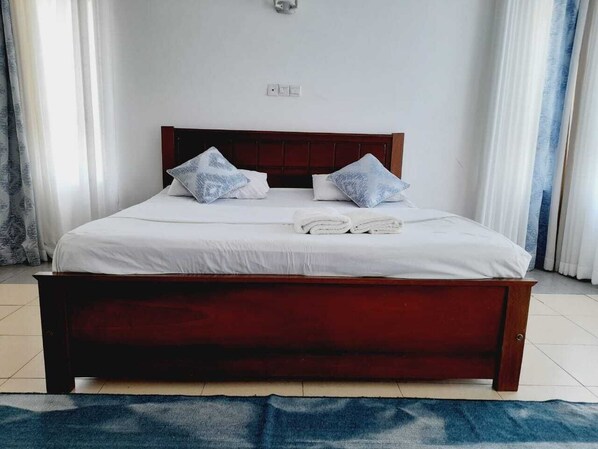 Un lit bien fait, avec un cadre en bois, une literie blanche et deux coussins décoratifs.