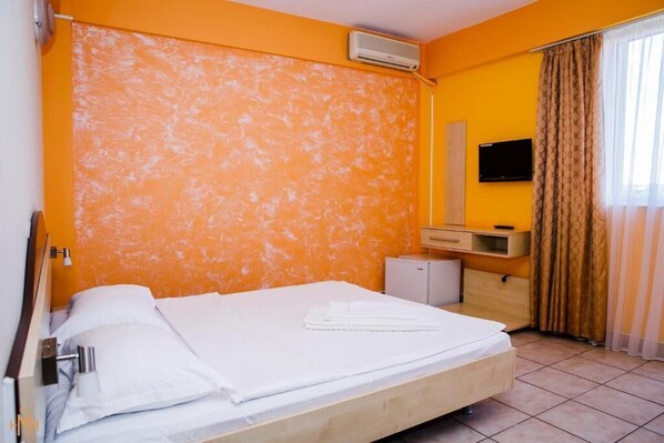 A hotel room with a bed, a small desk, a mirror, and an air conditioning unit.