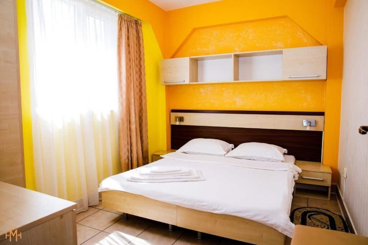 Hotellihuone, jossa on sänky, yöpöytä ja sängyn yläpuolella oleva sisäänrakennettu hylly.