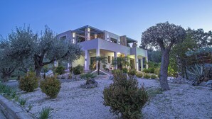 A modern house with a flat roof, large windows, and a garden with various plants and trees.