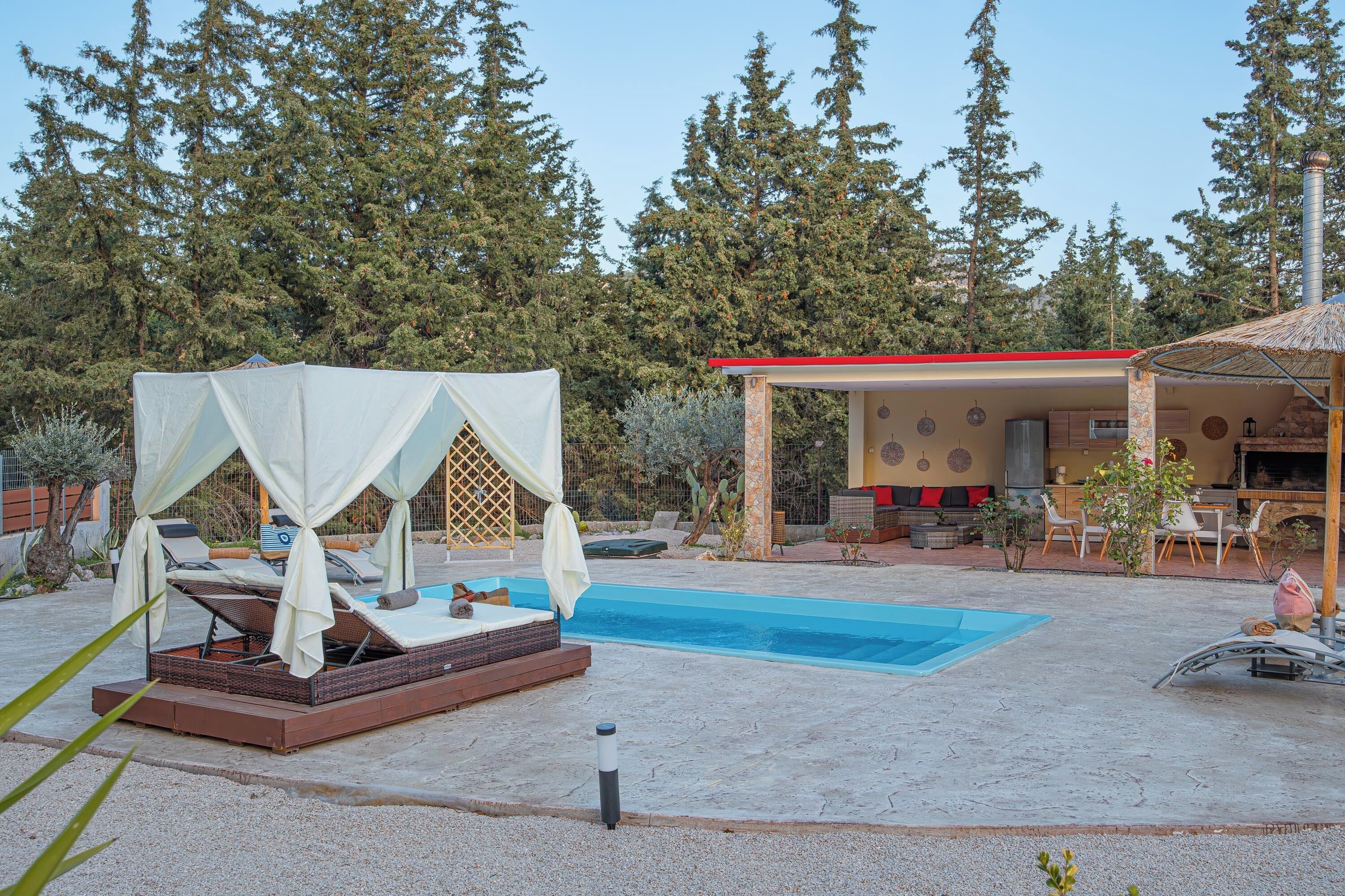 A pool area with a hot tub, a covered seating area, and a building with a chimney.