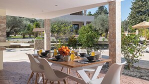 An outdoor dining area with a table set for four, surrounded by white chairs, with a view of a modern building and trees in the background.