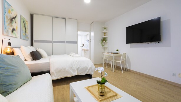 Una habitación de hotel moderna con cama, una zona de estar con mesa y sillas, televisor montado en la pared y obras de arte en las paredes.