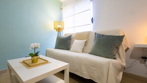 Una habitación acogedora con un sofá blanco, una mesita con una bandeja y una planta en maceta, además de una lámpara.