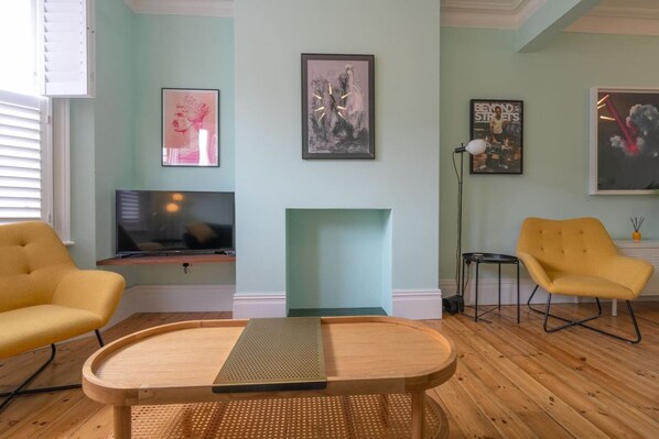 A living room with a TV, two yellow chairs, a wooden coffee table, and artwork on the walls.
