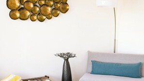 Ett vardagsrum med en grå soffa, ett runt soffbord, gråa sittpuffar, en guldfärgad spegel som hänger på väggen och en hög golvlampa.
