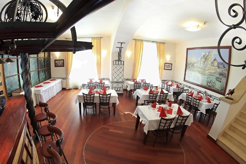 Un comedor con mesas dispuestas para el servicio, una zona de bar con taburetes y una escalera que conduce a un nivel superior.