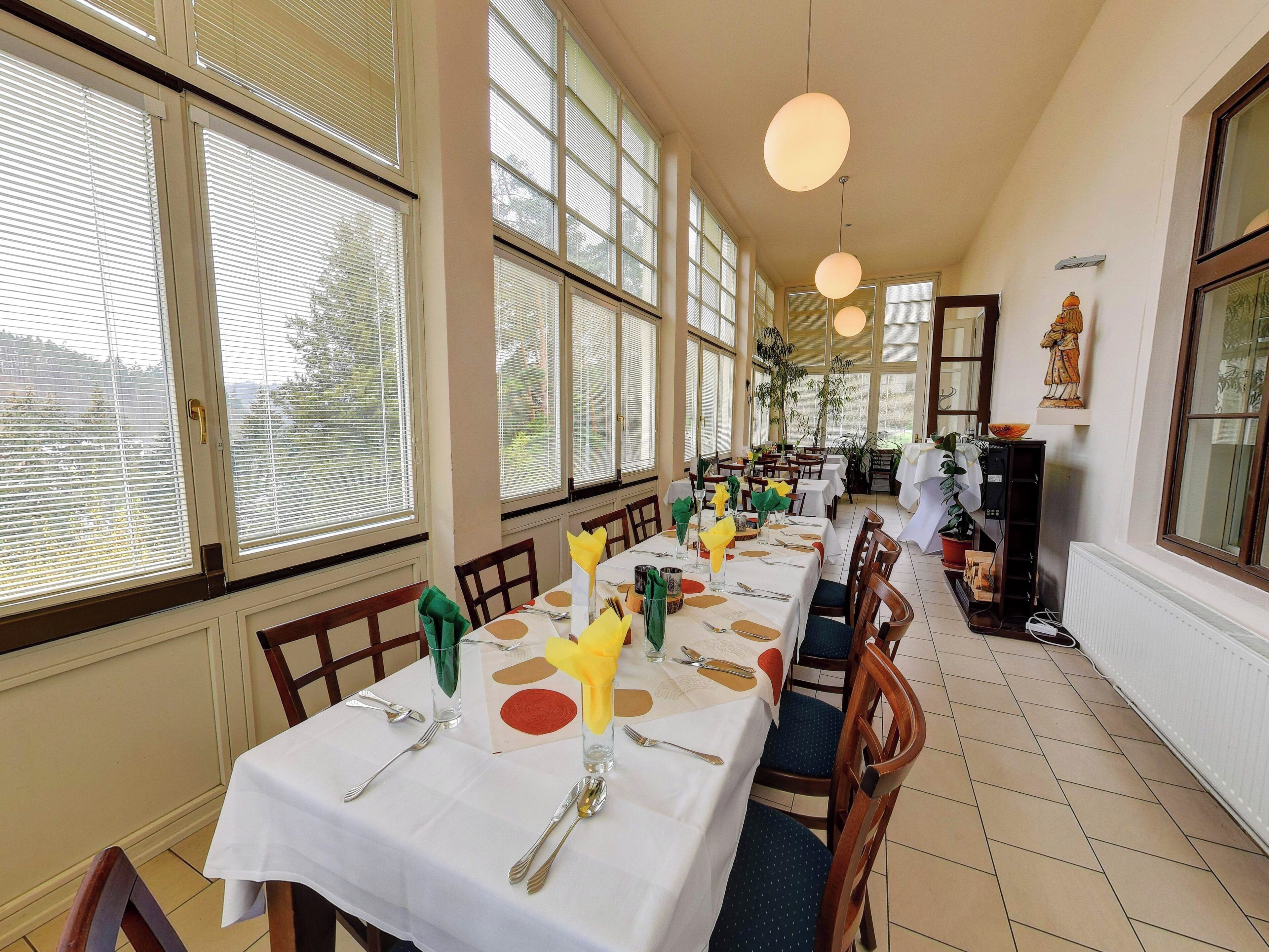 A dining area with tables set for a meal, large windows, and a statue on the wall.