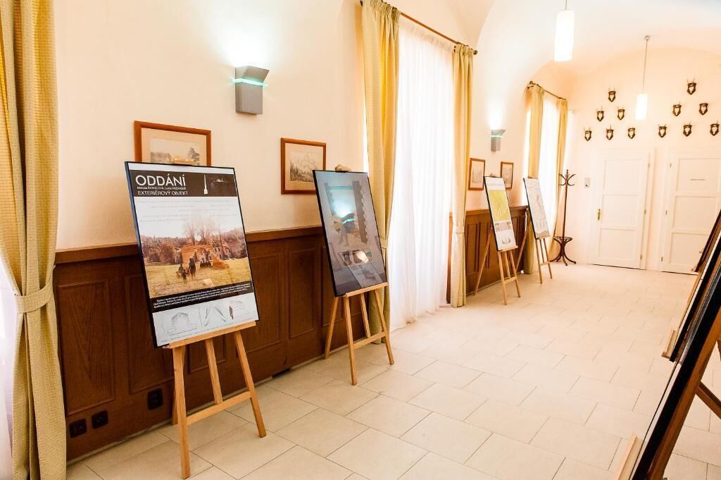 A hotel corridor with framed pictures on the walls, easels with paintings, and a wooden floor.